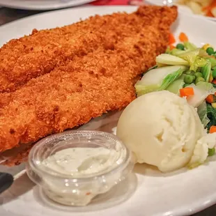 a plate of fried fish, mashed potatoes, and vegetables