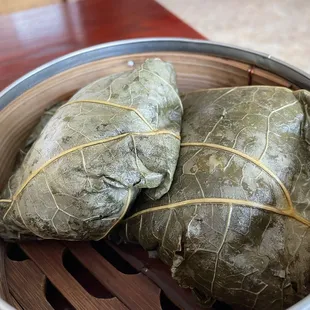 three wrapped grape leaves in a bamboo basket