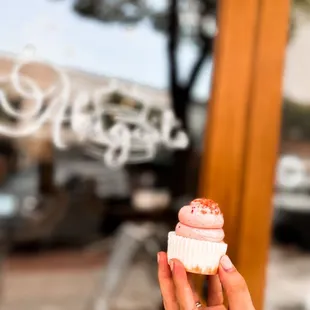 a person holding a cupcake in front of a window