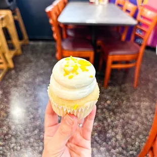 a hand holding a cupcake with frosting and sprinkles