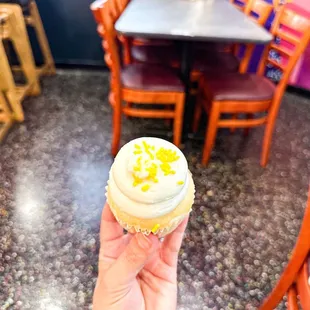 a hand holding a cupcake with white frosting and sprinkles