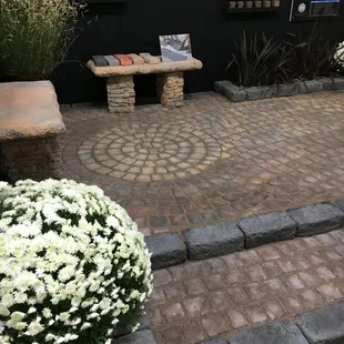 a brick patio with a bench and flowers