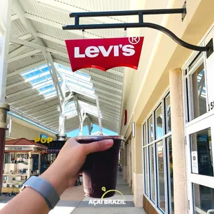 a hand holding a drink in front of a levi's sign
