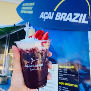 a hand holding a cup of ice cream and strawberries