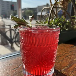 a red drink with a sprig of sage