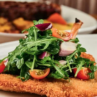 Pork Chop Milanese -  breaded berkshire pork chop on the bone, arugula, grape tomatoes, red onion