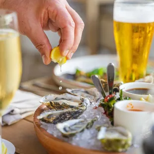 a person sprinkling lemon over a plate of oysters