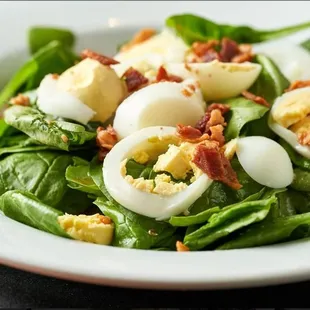 a spinach salad with hard boiled eggs and bacon