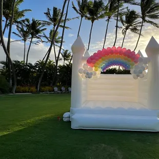 Rainbow theme balloon garland on White Castle bounce house for a child's birthday celebration.