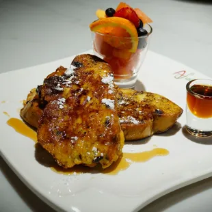 a plate of french toast with fruit and syrup