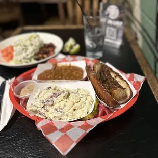 Bratwurst on a toasted pretzel bun with caramel onions, potato salad and amazing baked beans