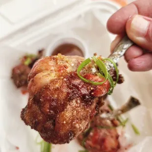 a hand holding a piece of meat in a styrofoam container