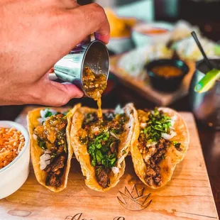 a person pouring sauce onto tacos