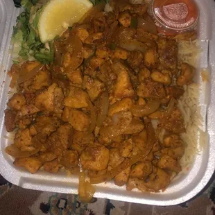 a tray of chicken and rice with a lemon wedge