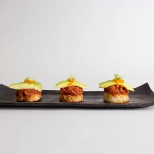 three pieces of sushi on a black plate