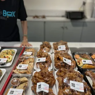 a woman standing in front of trays of donuts
