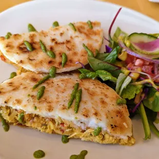 Arepa sandwich. Corn cake filled with shredded chicken and creole sauce, topped with cilantro sauce. Served with a salad