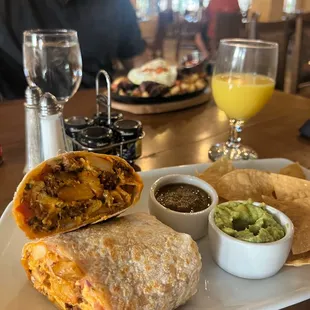 a burrito, chips, salsa, and a glass of orange juice