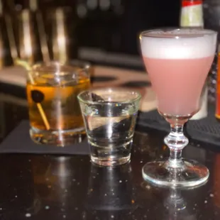 a shot of a pink drink and two shot glasses on a bar counter