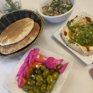  plate of pita bread, a bowl of olives, a bowl of pickles, and a bowl of