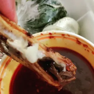 a person dipping a piece of meat into a bowl