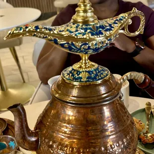a woman sitting at a table with a teapot on top of it