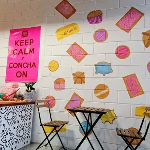 a table and chairs in front of a wall with a sign that says keep calm and concha on