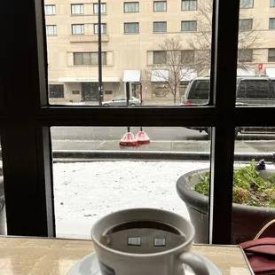 a cup of coffee on a table in front of a window