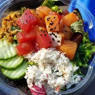 Poke bowl with salmon, tuna, cucumbers, crab salad, green salad, seaweed salad, crispy onions