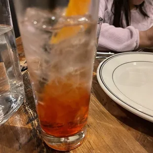 a little girl sitting at a table with a glass of water and an orange slice