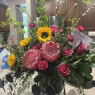 Beautiful fresh arrangement with protea, roses, ranunculus, greenery and willow. Gorgeous keepsake container.