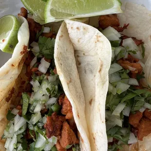 Tender, juicy Al Pastor tacos on flour tortilla, cut to just the right size, with diced cilantro, onion, and lime wedges.