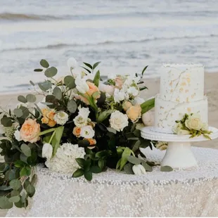 a wedding cake and flowers on a table on the beach