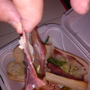 a person grabbing a piece of meat from a sandwich