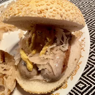 Kielbasa on sesame kaiser roll with brown mustard and sauerkraut.