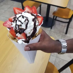 a hand holding a cone with strawberries and chocolate