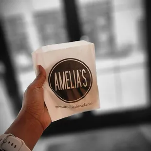  a hand holding a paper bag with the name amelia&apos;s