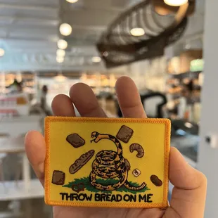  a hand holding a patch that says throw bread on me