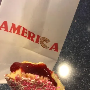 a hand holding a donut with pink sprinkles