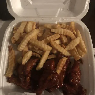 a styrofoam takeout container filled with chicken wings and french fries