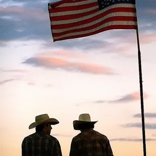 two men in cowboy hats looking at the american flag