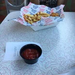 a woman sitting at a table with french fries and ketchup