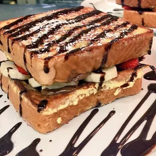 Stuffed French toast with Nutella strawberries and bananas a drizzle of chocolate syrup and powdered sugar a party in my mouth