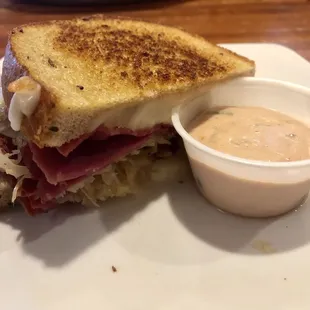 Half of a Reuben sandwich with sauce sauce on the side.