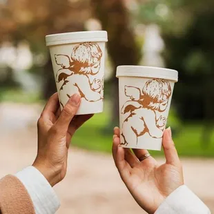 two people holding coffee cups in their hands