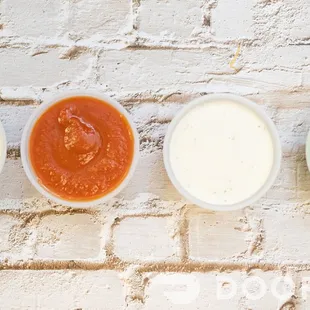 four different sauces in bowls on a brick wall