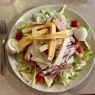 a plate of salad with ham, cheese, tomatoes, lettuce, and hard boiled eggs