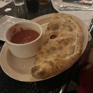 a piece of pizza and a bowl of tomato sauce