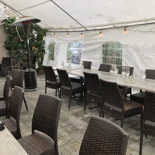 Outdoor dining in back of restaurant under large tent with heat lamps.