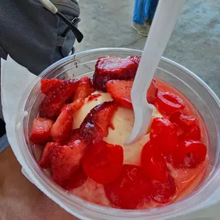 a person holding a plastic bowl of ice cream and strawberries